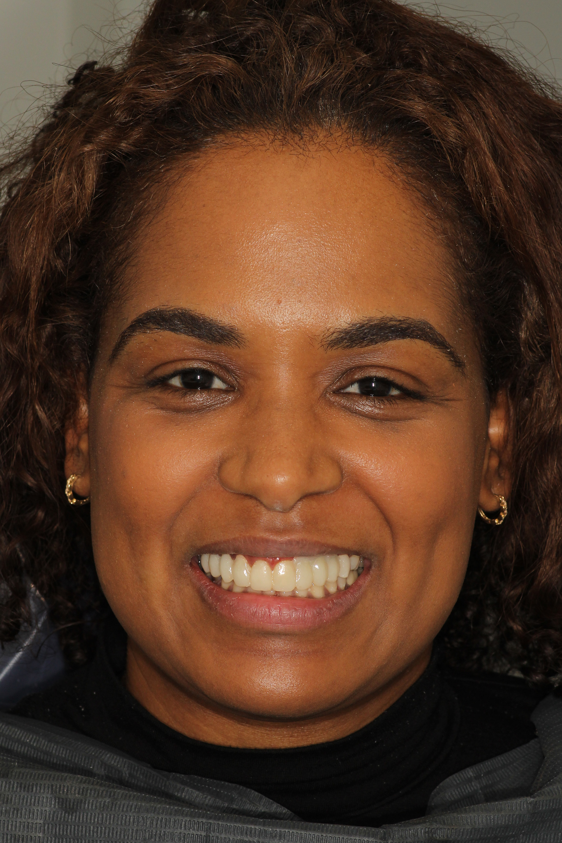 The image shows a smiling woman with short hair, wearing a black top, posing for a portrait with a neutral background.