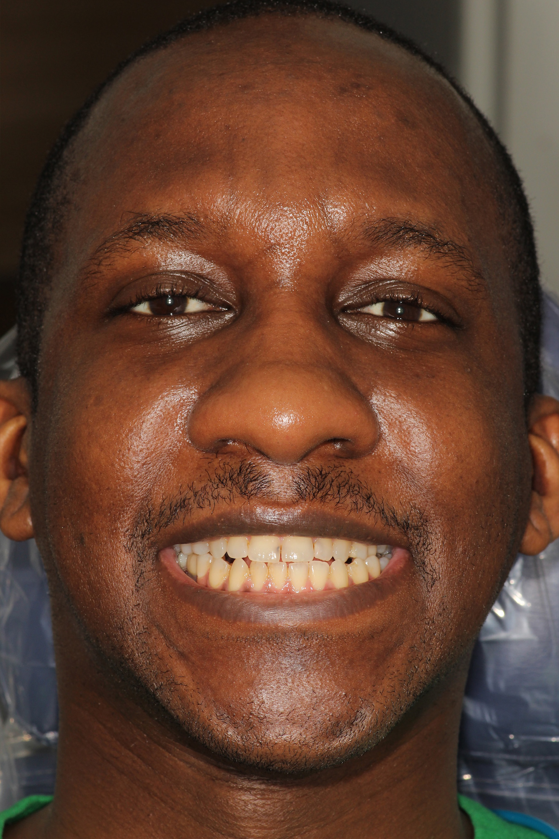 The image shows a man with a mustache smiling broadly at the camera, set against a water bottle background.