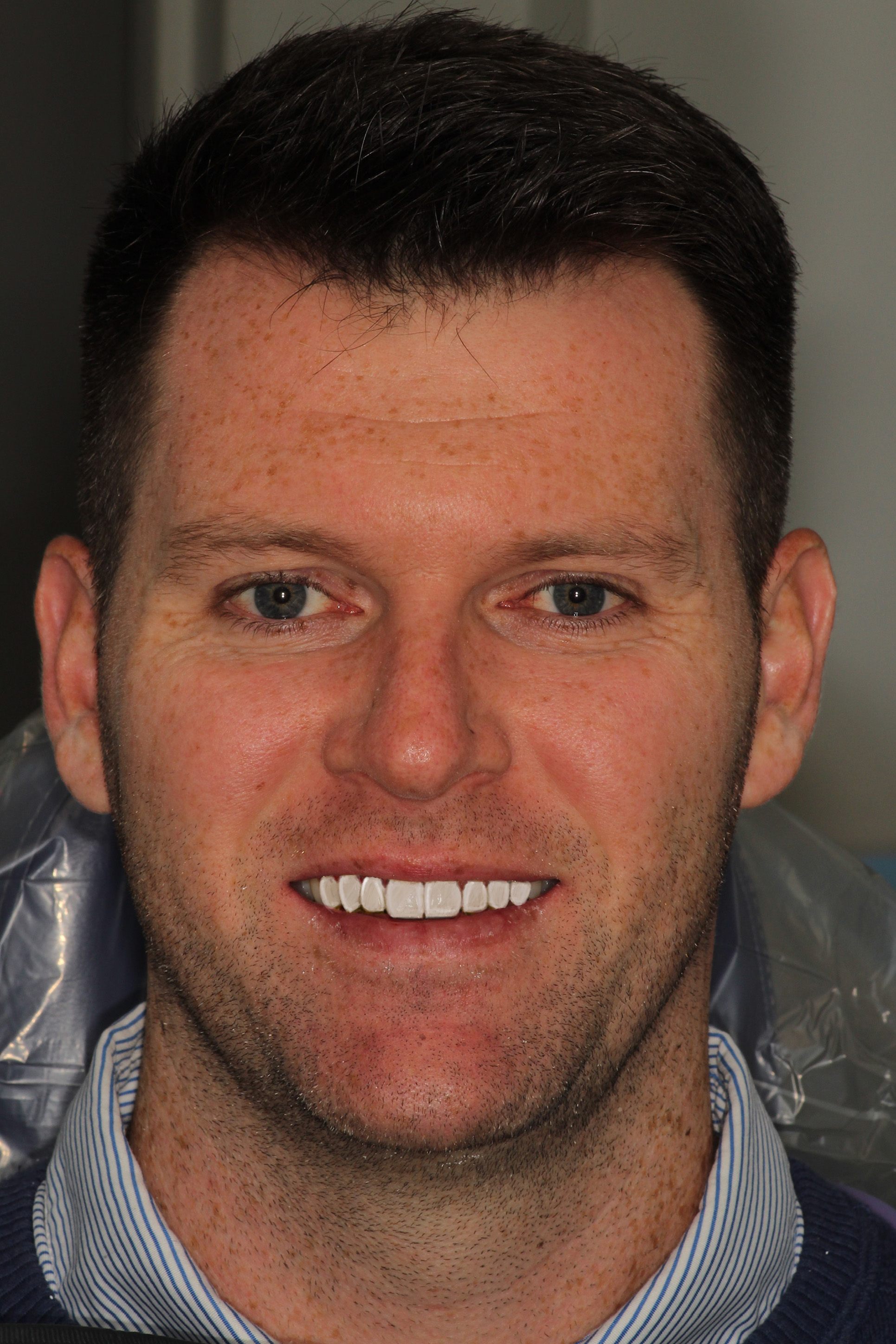 The image shows a man with short hair smiling at the camera.