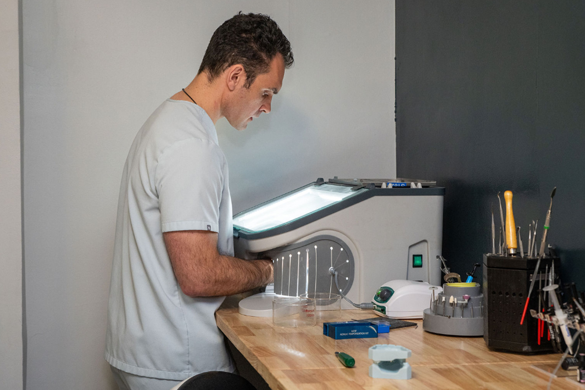 The image shows a man standing at a counter with various items, such as bottles and a computer monitor, suggesting he might be involved in some kind of scientific or technical work.