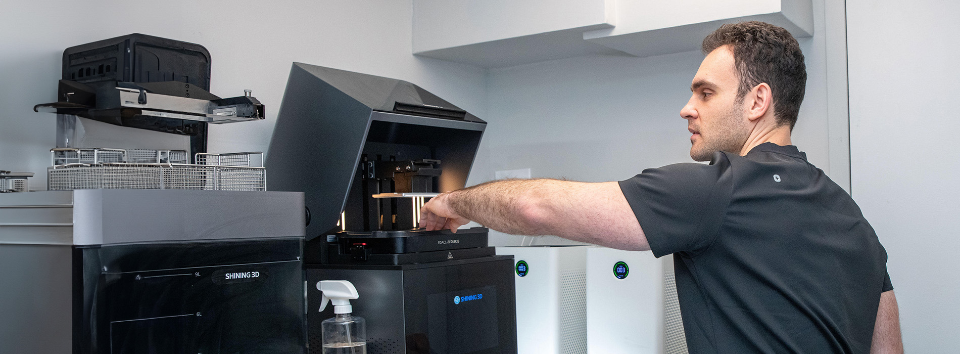 The image shows a man standing next to a printer in an office environment.